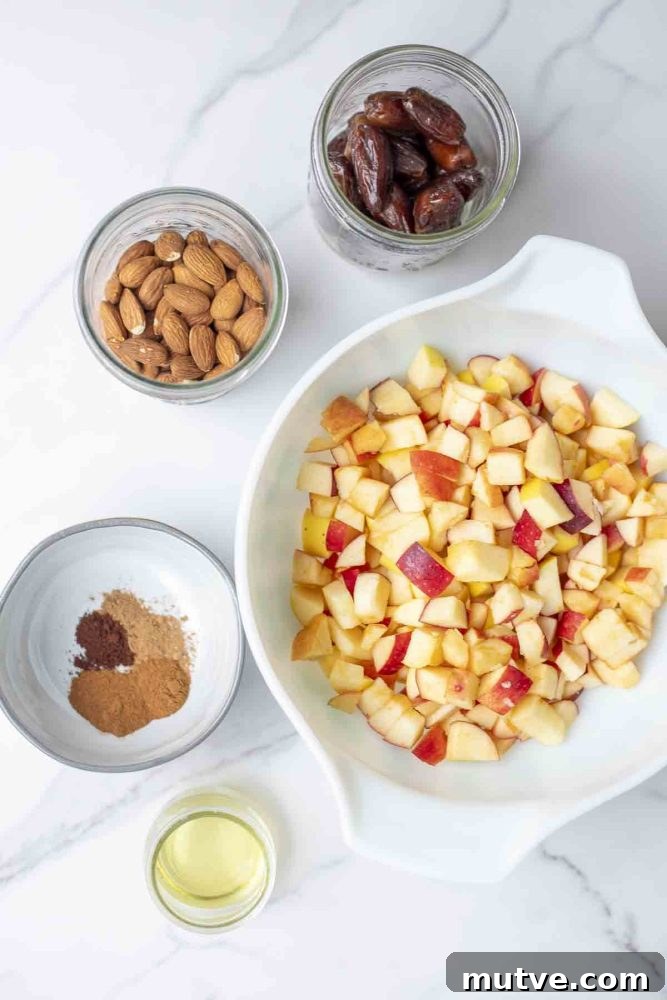 Gluten-Free Apple Crisp Recipe with Oat Crumble 6 bowls and jars filled with apples, dates, almonds, spices and oil on a marble countertop