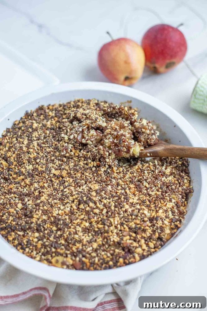 Gluten-Free Apple Crisp Recipe with Oat Crumble 7 a pie plate full of healthy apple crisp topped with dates and almonds on a marble counter with apples in the background