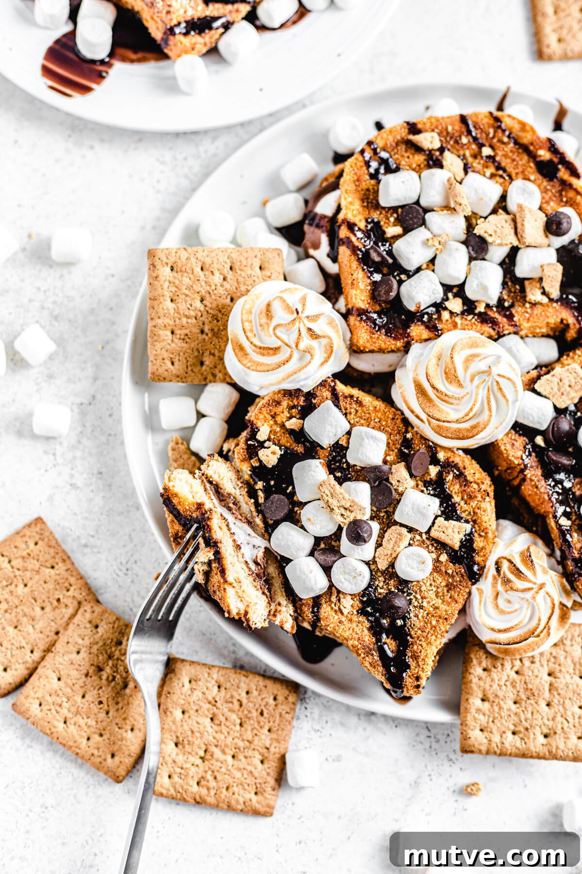 Campfire S'mores French Toast with Chocolate and Marshmallows 3 French toast on a white platter with a piece taken off of one