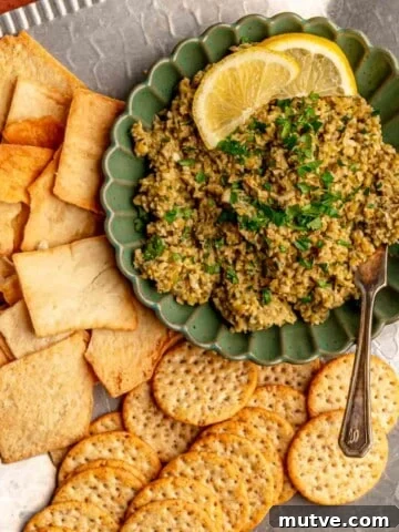 Olive tapenade in a bowl garnished with lemon wedges and with crackers.