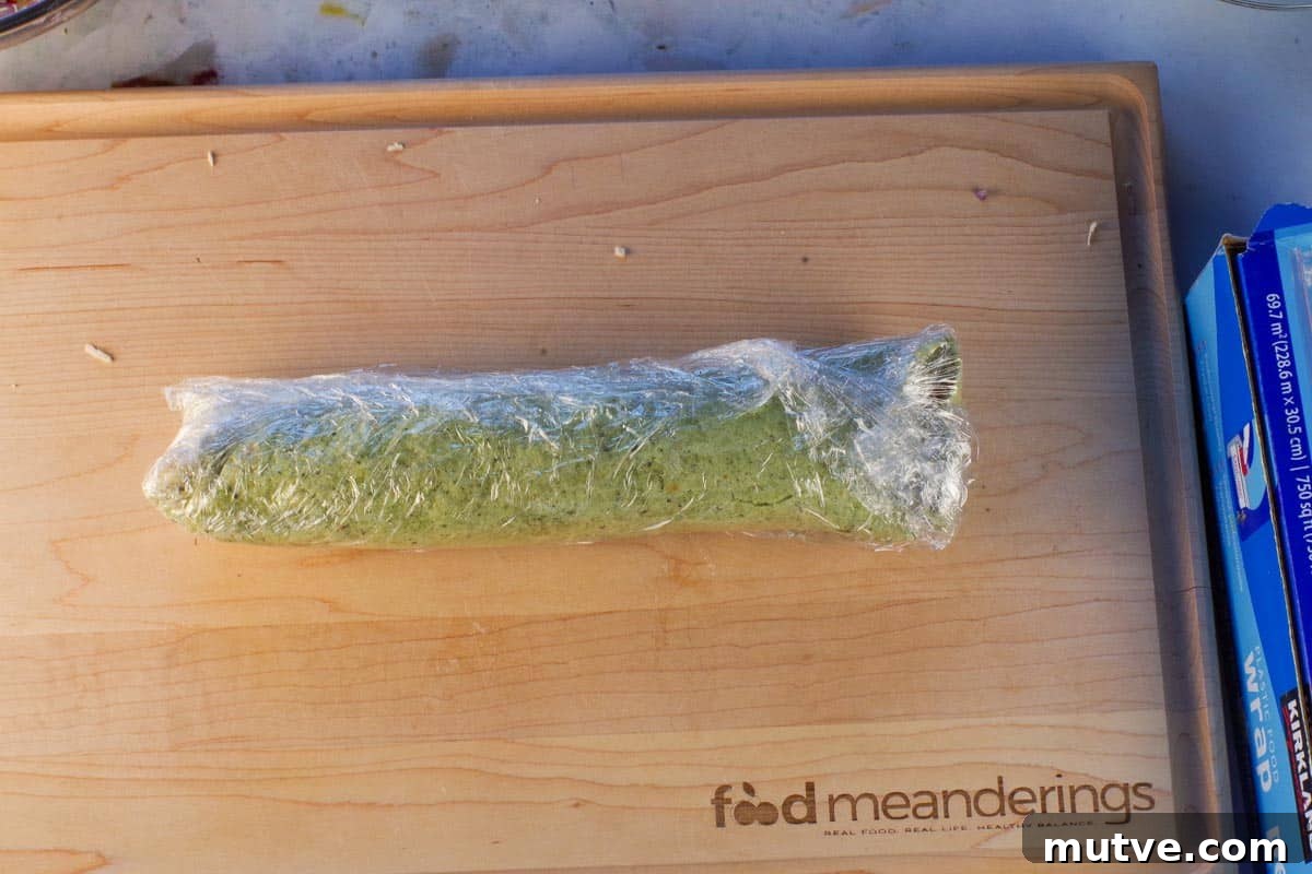 Chicken Tortilla Pinwheels Recipe: Cheesy Party Appetizer 12 Filled and rolled tortilla wrapped in plastic wrap, on a wooden cutting board.