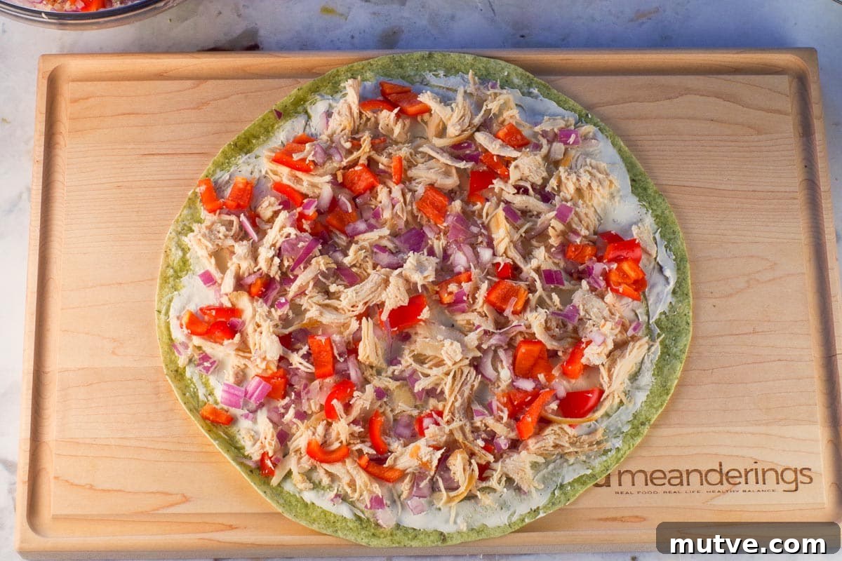 Chicken Tortilla Pinwheels Recipe: Cheesy Party Appetizer 8 Chicken mixture spread on tortilla on wooden cutting board.