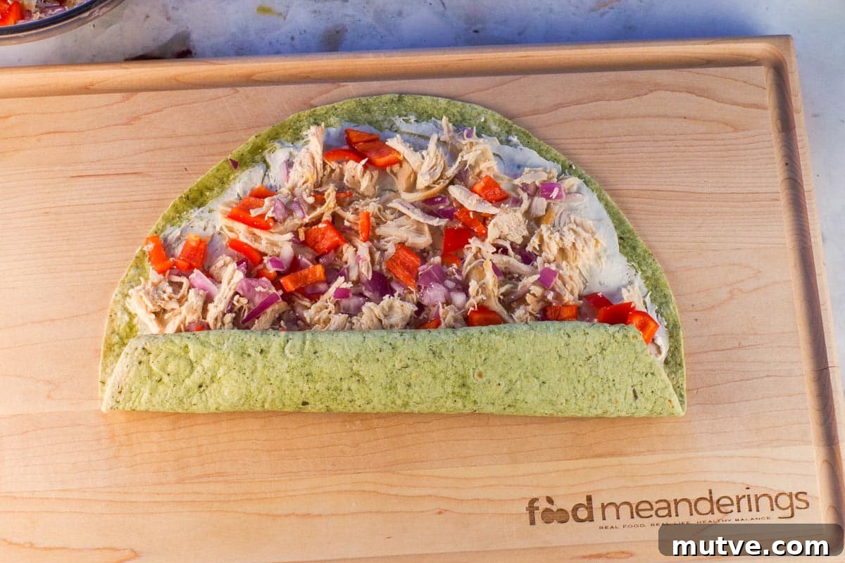Chicken Tortilla Pinwheels Recipe: Cheesy Party Appetizer 9 Chicken tortilla pinwheels being rolled up from bottom on wooden cutting board.