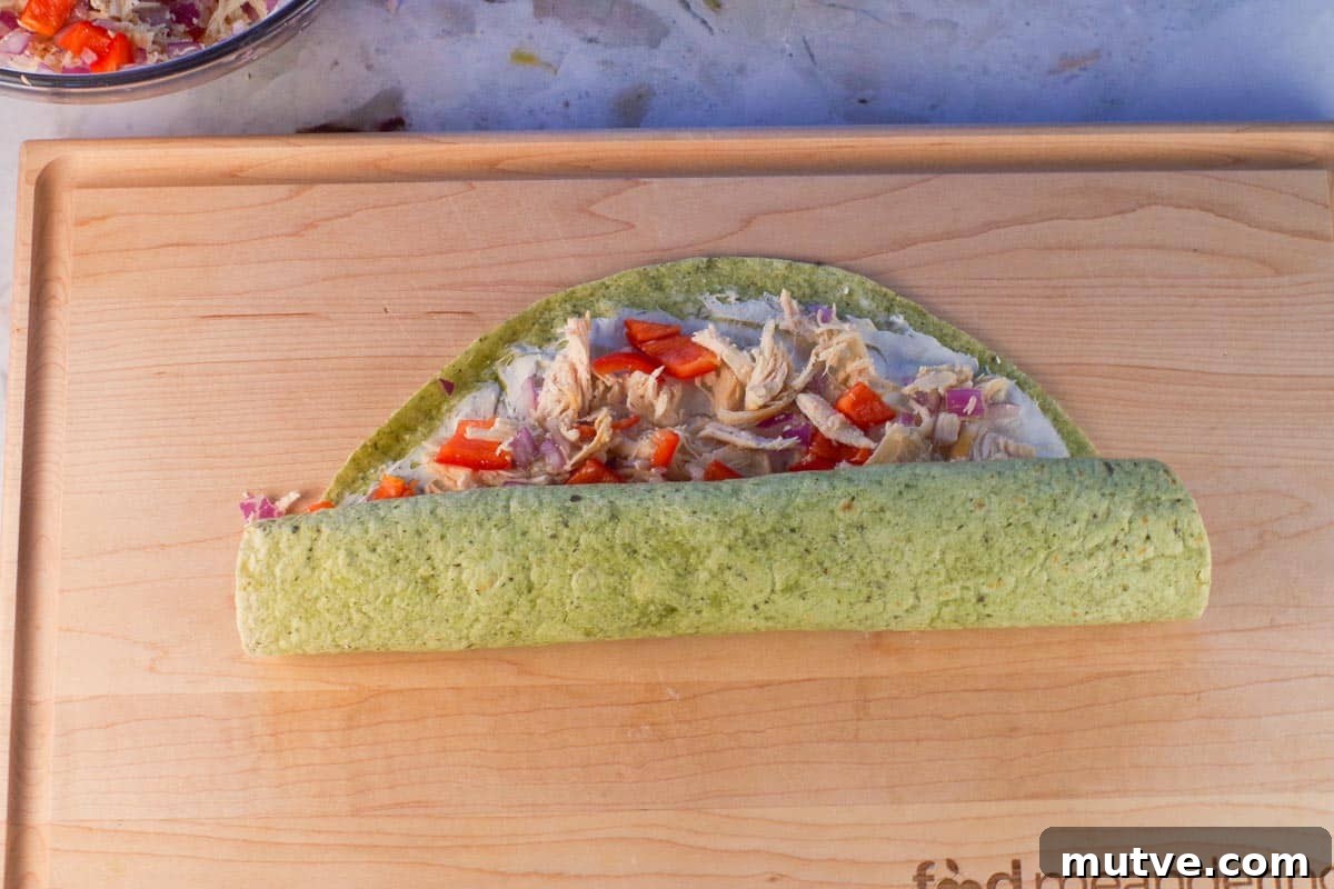 Chicken Tortilla Pinwheels Recipe: Cheesy Party Appetizer 10 Chicken Tortilla being rolled up to near the top on wooden cutting board.