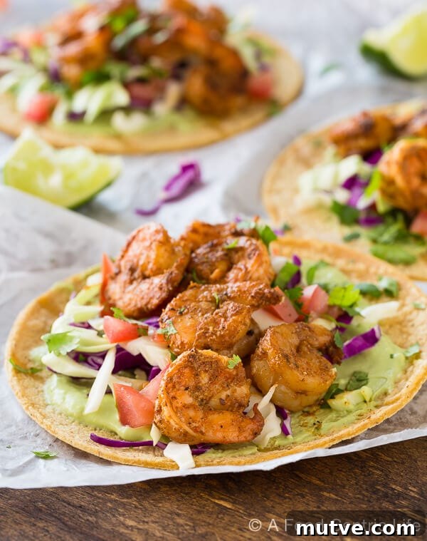Baja Shrimp Tacos: Grilled or Stovetop 2 Grilled shrimp tacos piled on white paper on a wood table, with avocado sauce and veggies.
