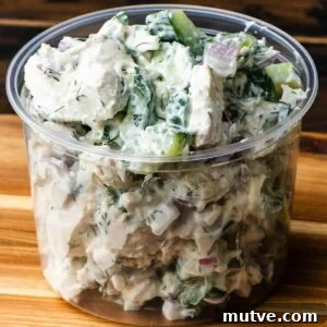 Creamy chicken cucumber salad in deli container on wooden board.