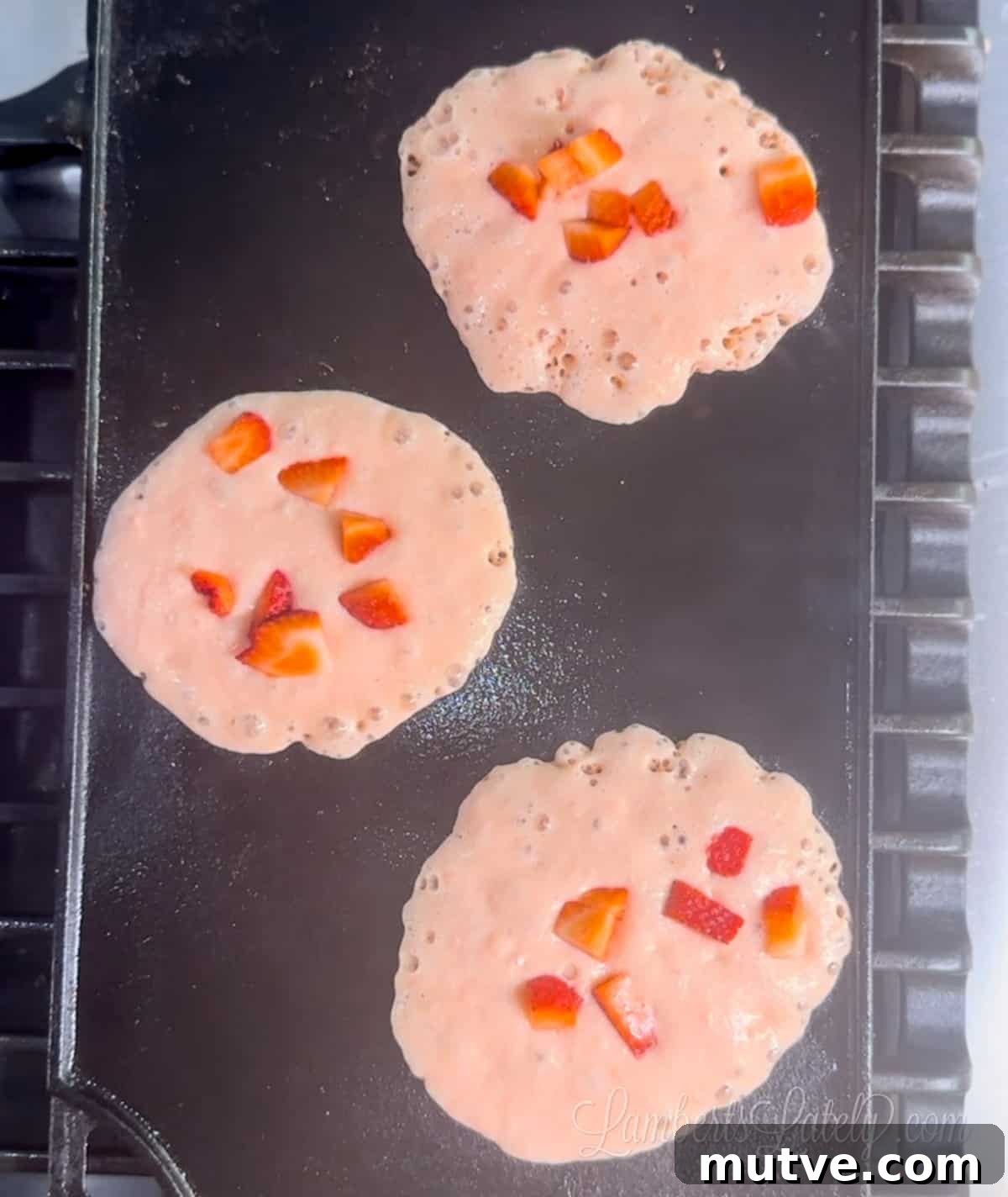 pink pancakes with strawberries on top on a griddle pan.