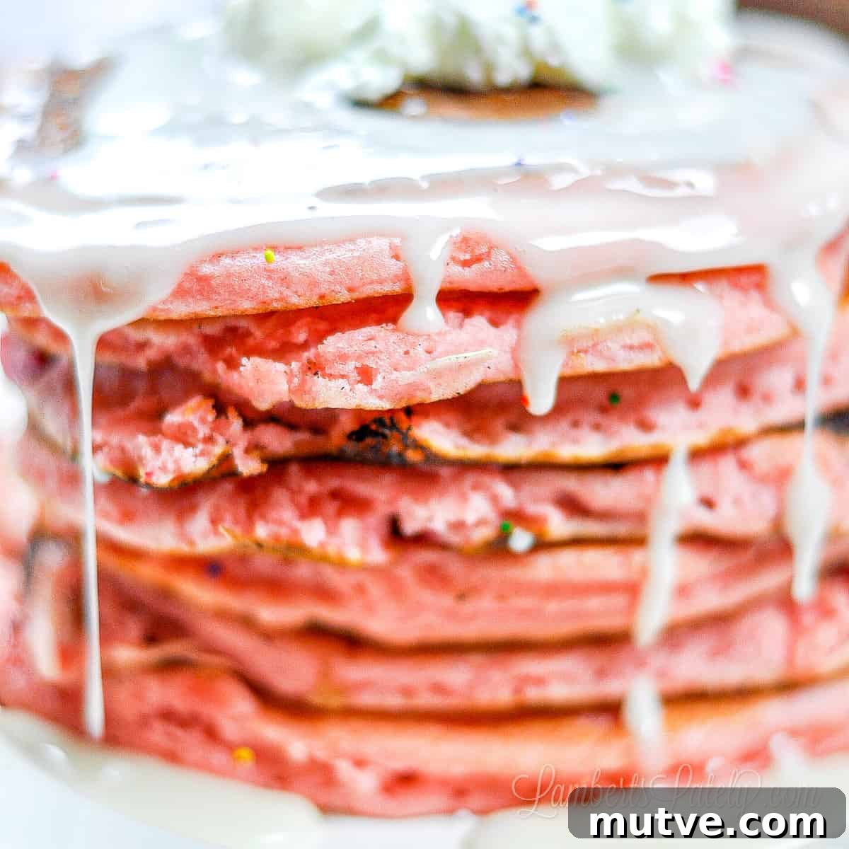 white icing syrup dripping off of a stack of pink pancakes.