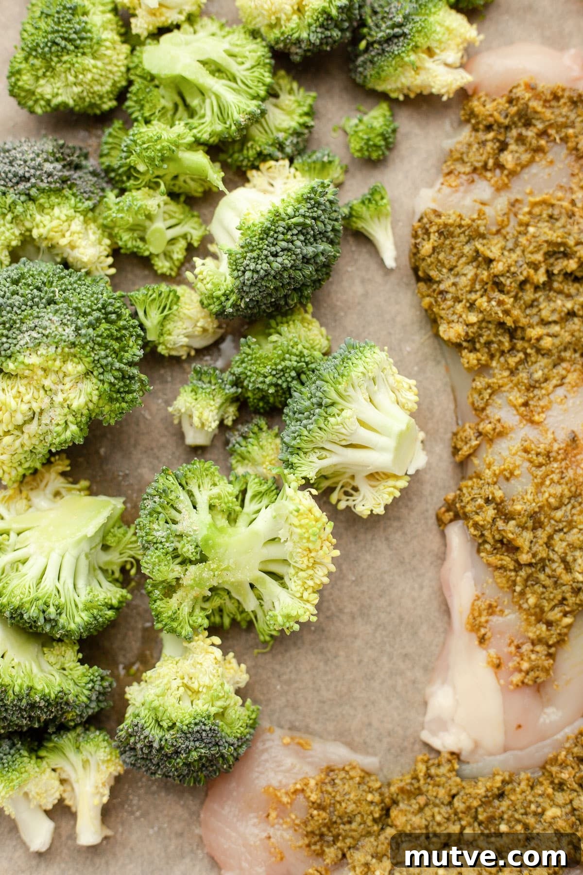 Sheet-Pan Pesto Chicken with Roasted Broccoli 4 Chicken breasts covered in pesto sit on a baking sheet with broccoli.
