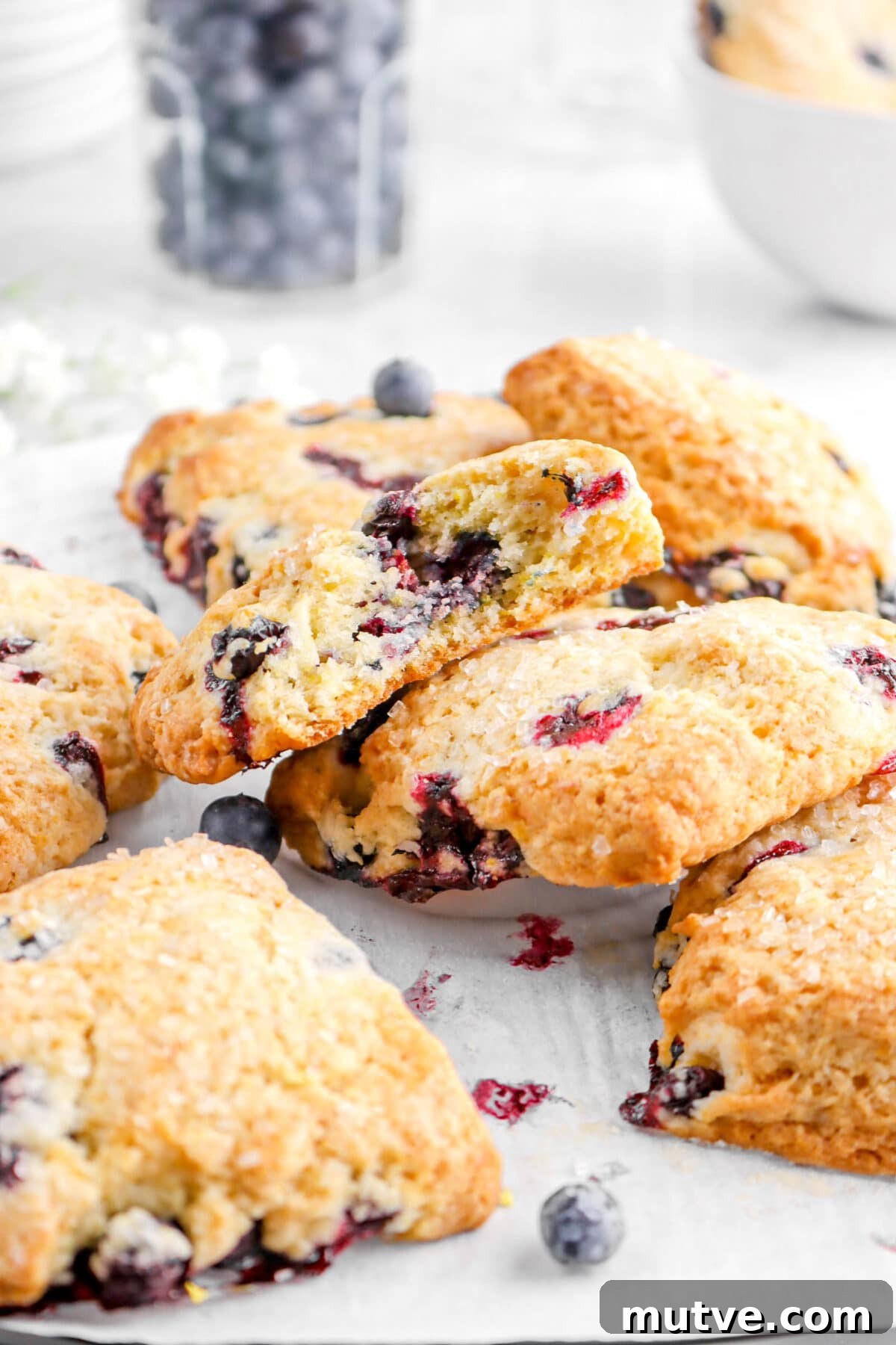 piled scones on parchment paper with jar of blueberries behind