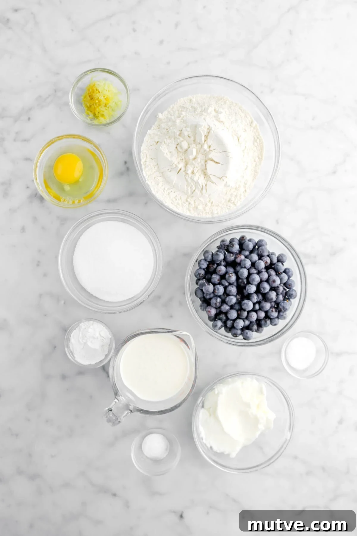 lemon zest, egg, flour, sugar, baking powder, milk, blueberries, salt, shortening, and baking soda on marble surface