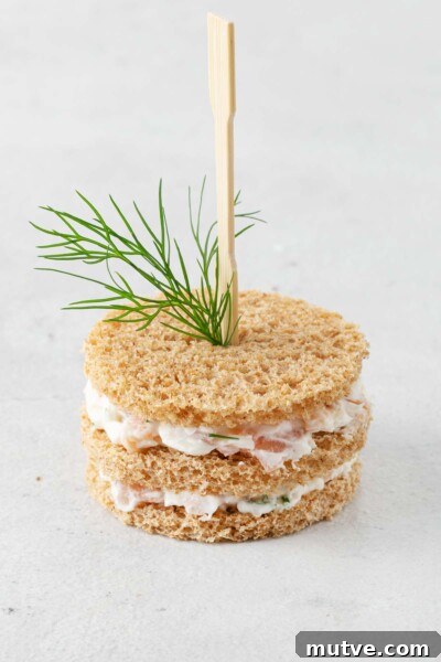 Smoked Salmon Tea Sandwiches Recipe with Cream Cheese and Dill 10 Bread cut into circles with layers of smoked salmon spread skewered with cocktail fork and fresh dill.