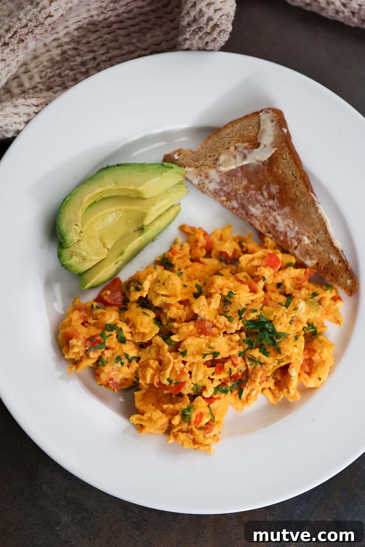 huevos pericos with a slice of toast and sliced avocado on the side.