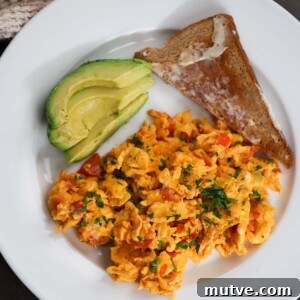 huevos pericos with a slice of toast and sliced avocado on the side.