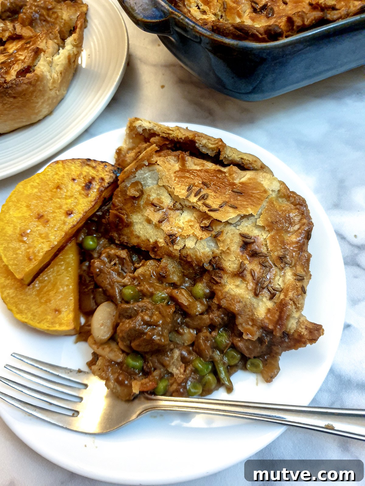 A slice of Moroccan lamb pie on a white plate with two slices of roasted butternut squash.