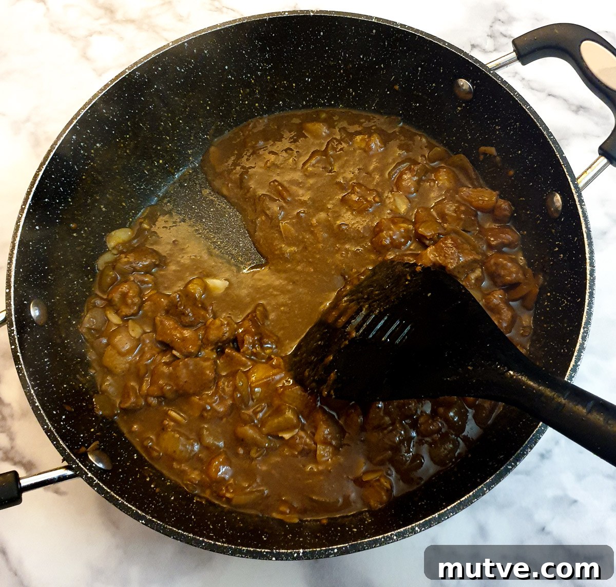 A spatula being drawn through the Moroccan lamb pie filling to show the consistency of the gravy.