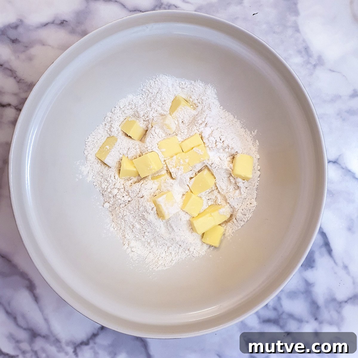 Cubed butter and flour in a large white mixing bowl.