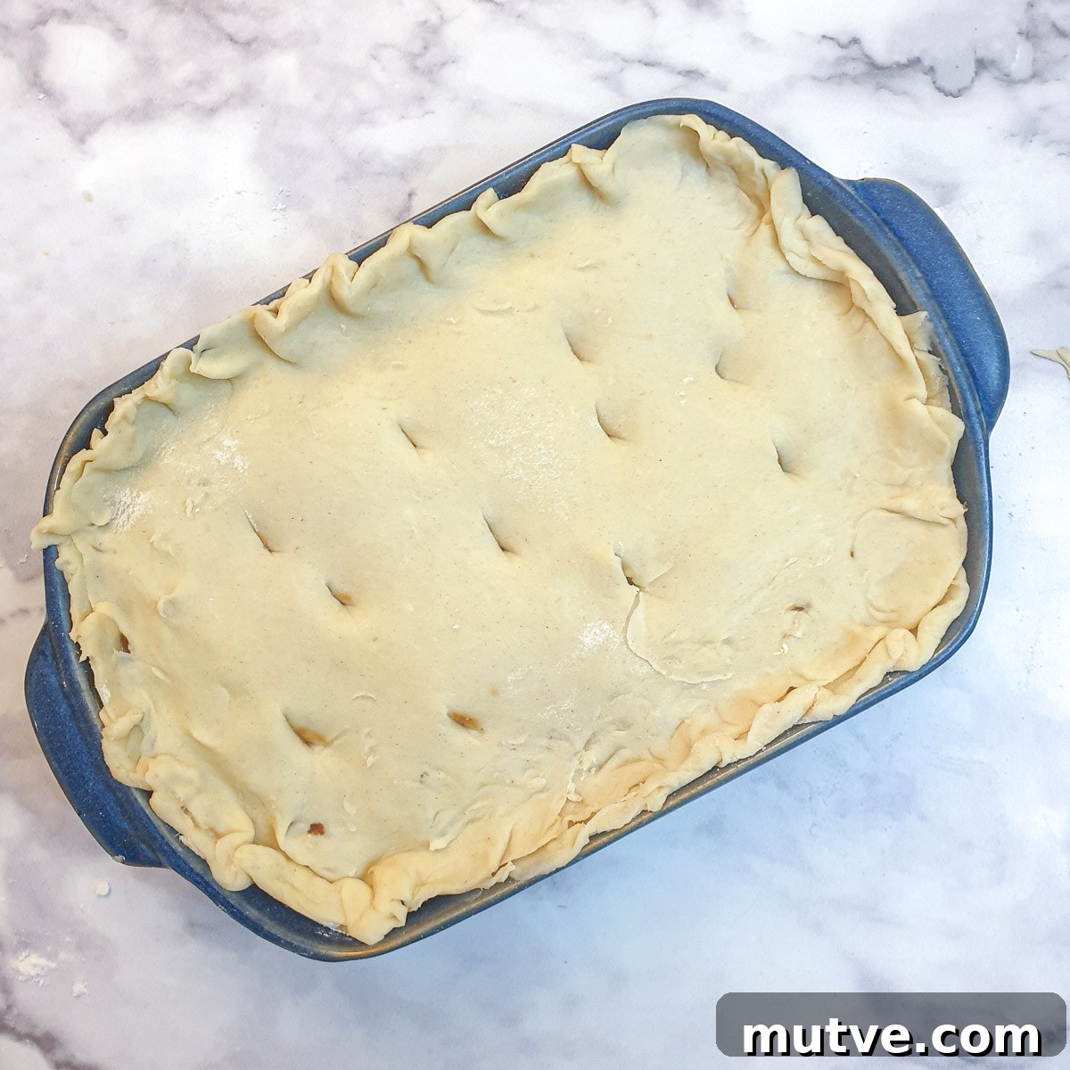An unbaked Moroccan lamb pie with the pastry lid added, in a blue baking dish.