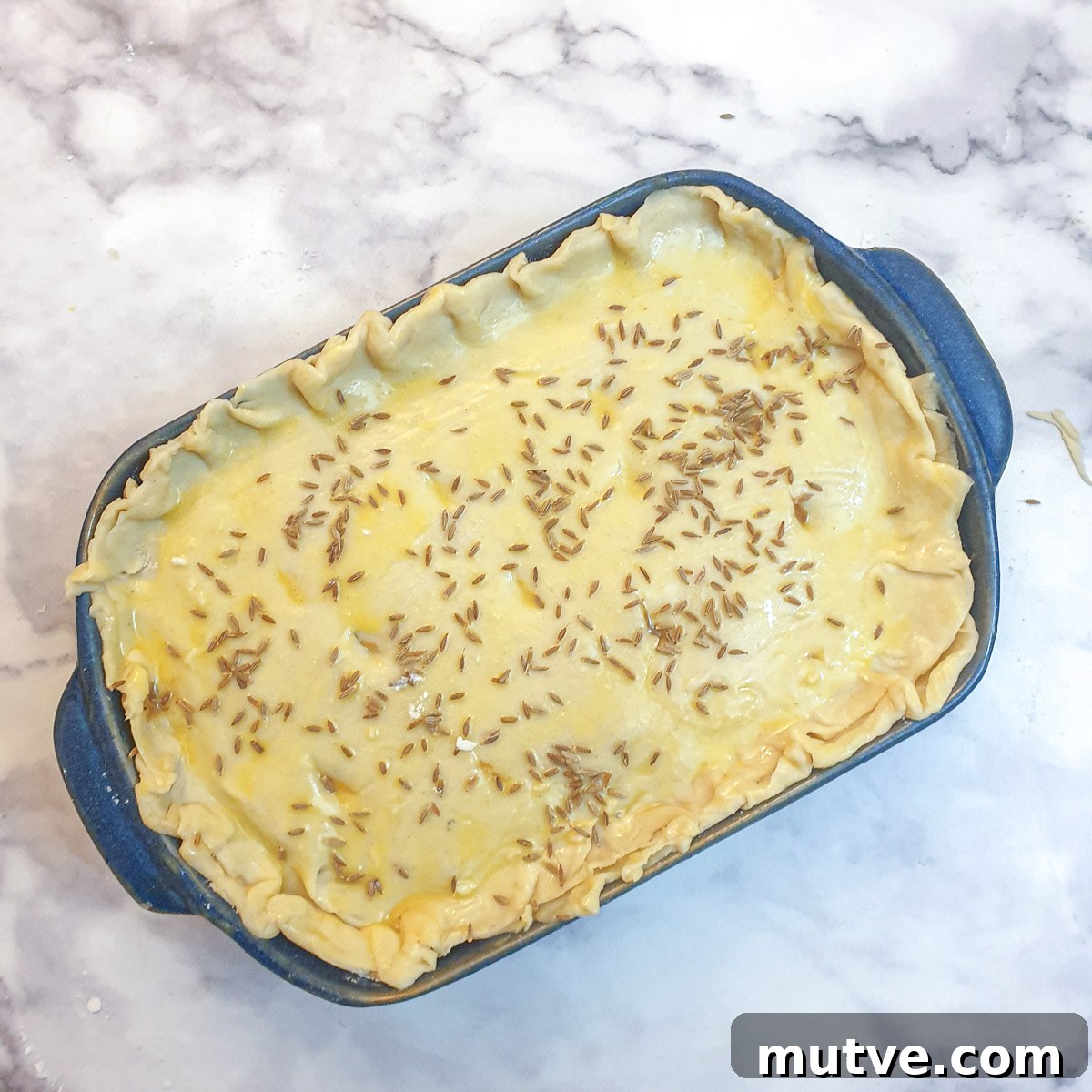 Moroccan lamb pie covered in egg wash and sprinkled with cumin seeds.
