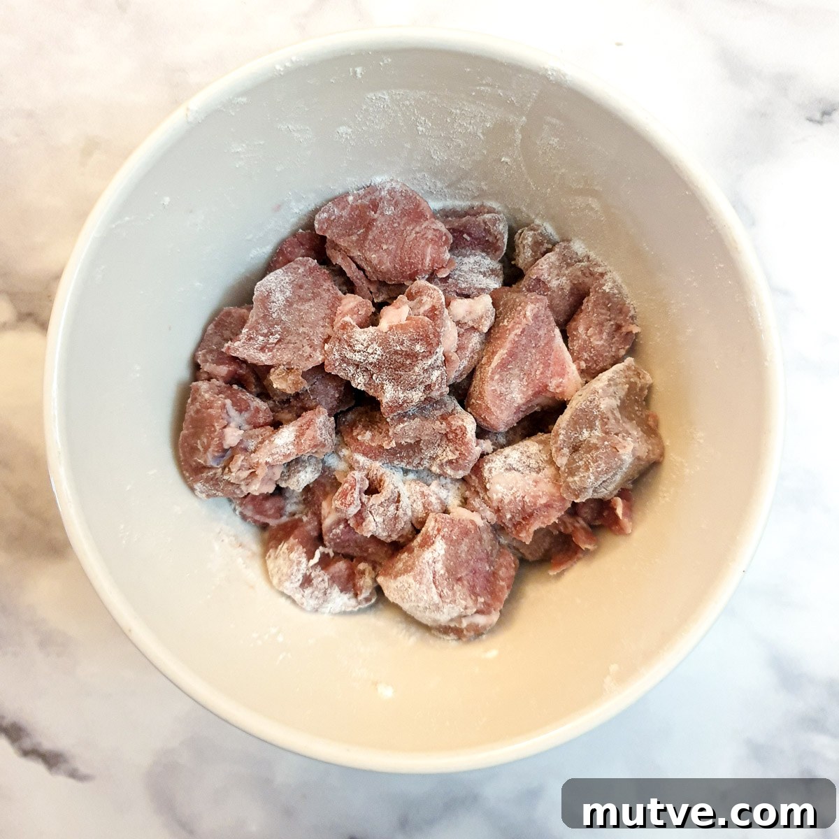 Cubes of lamb coated in flour in a small white mixing bowl.