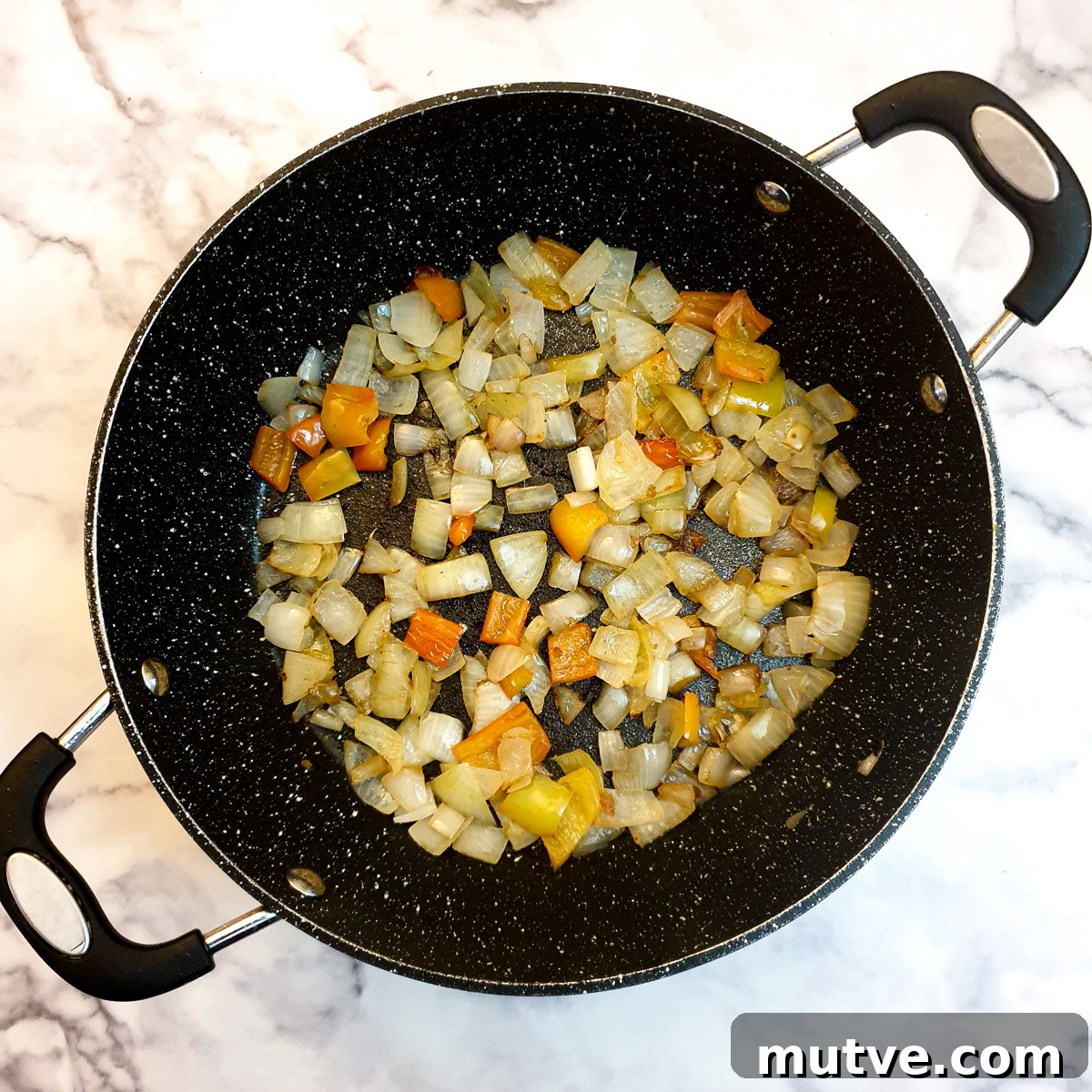 Onions and red pepper frying in a frying pan.