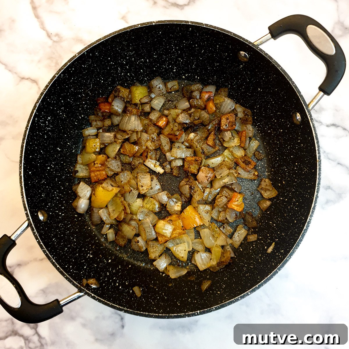 Ground spices mixed with onions and red peppers in a frying pan.