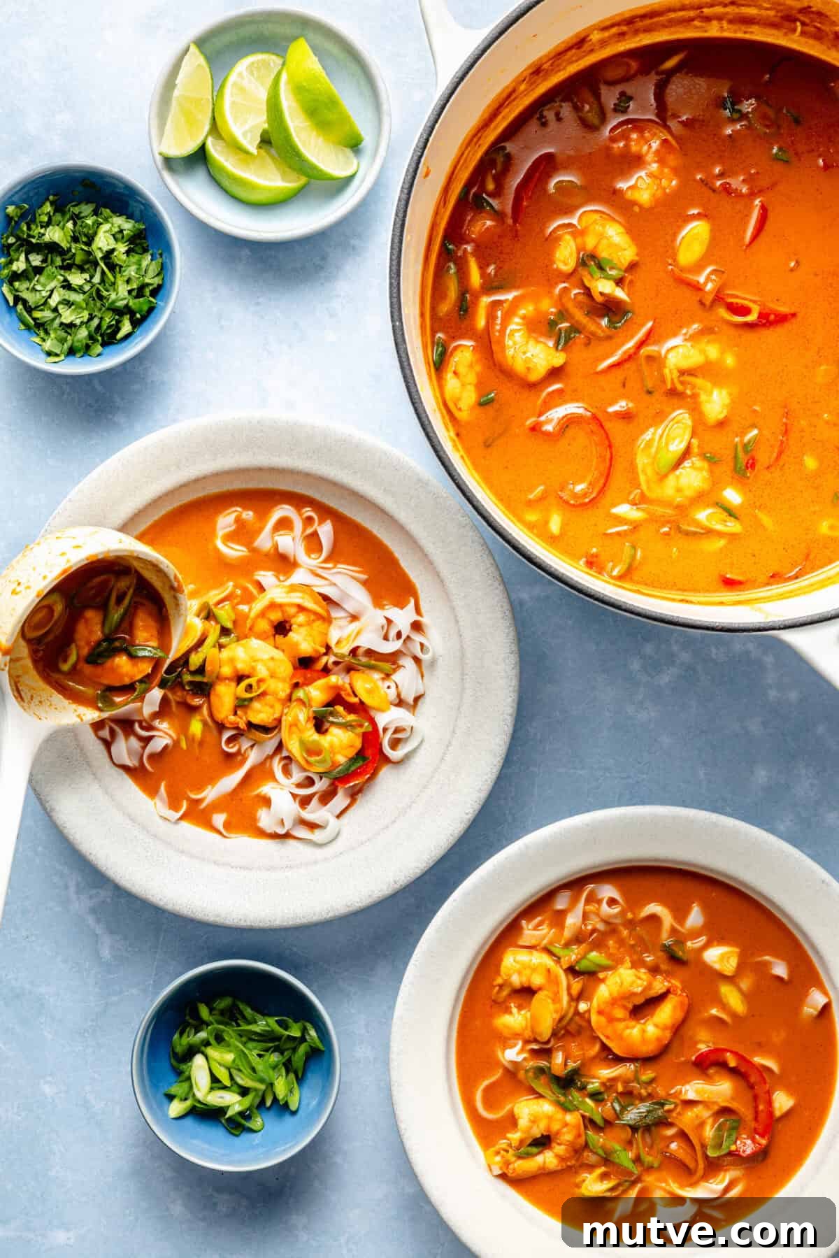 two bowls of gochujang and coconut shrimp noodle soup with a side of lime and herbs