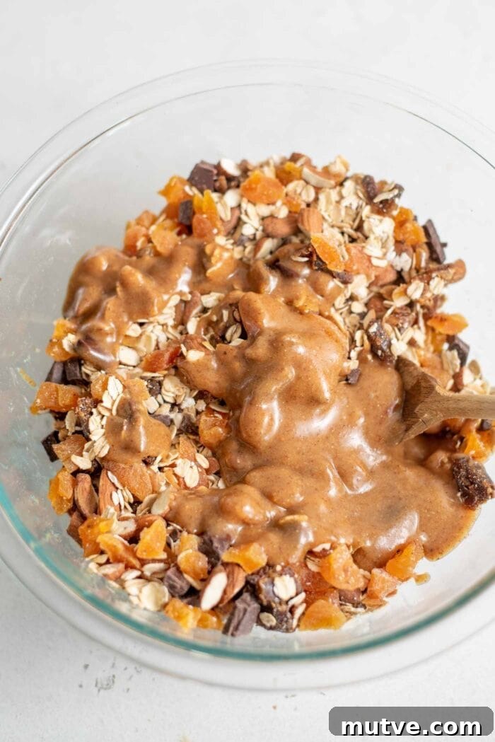 Homemade Apricot Muesli Granola Bars 8 Almonds, oats, dates, apricots and chocolate with maple syrup in a glass mixing bowl.