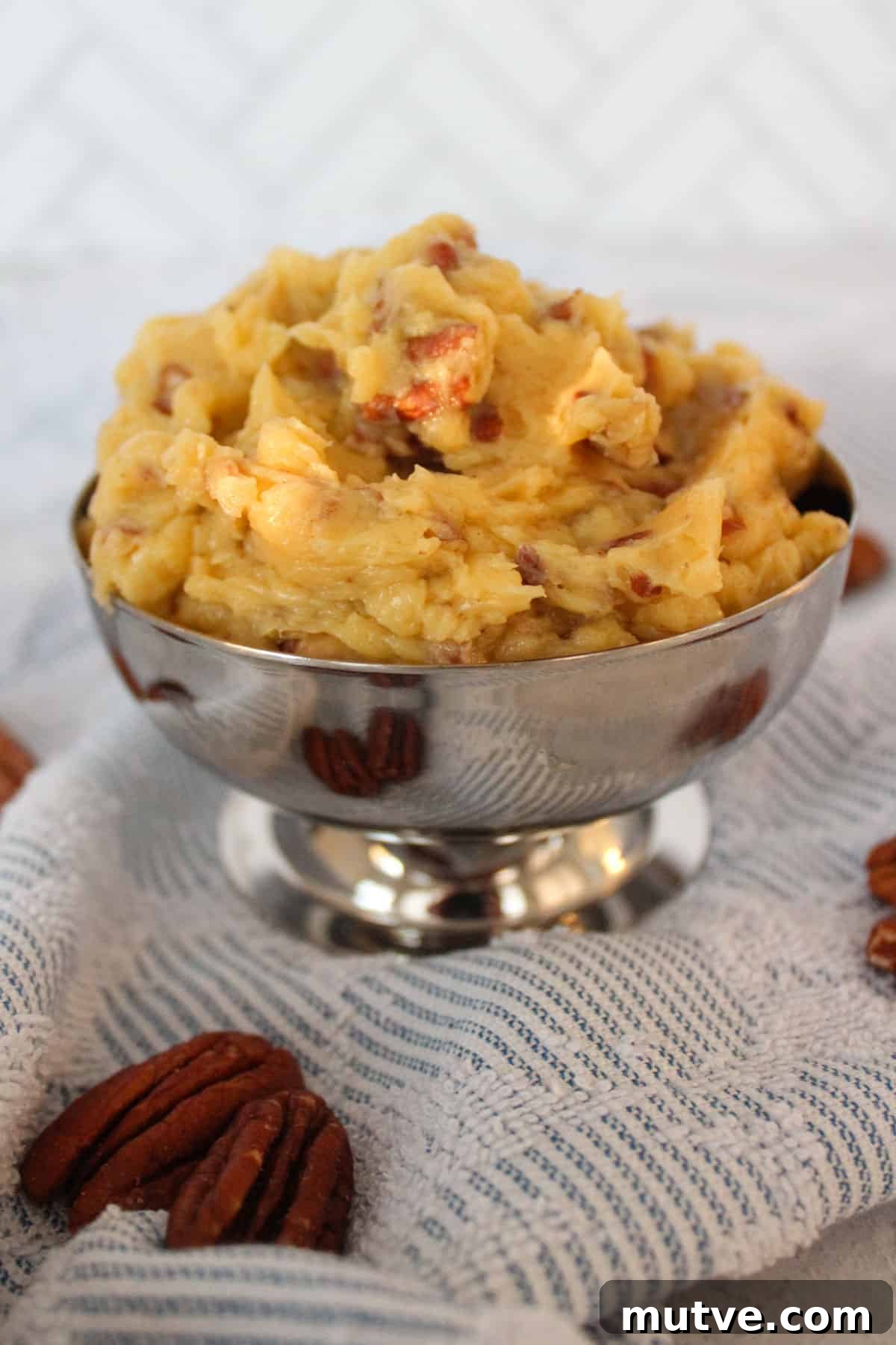 Honey pecan butter in a silver dish sitting on a blue and white towel with pecan halves around it.