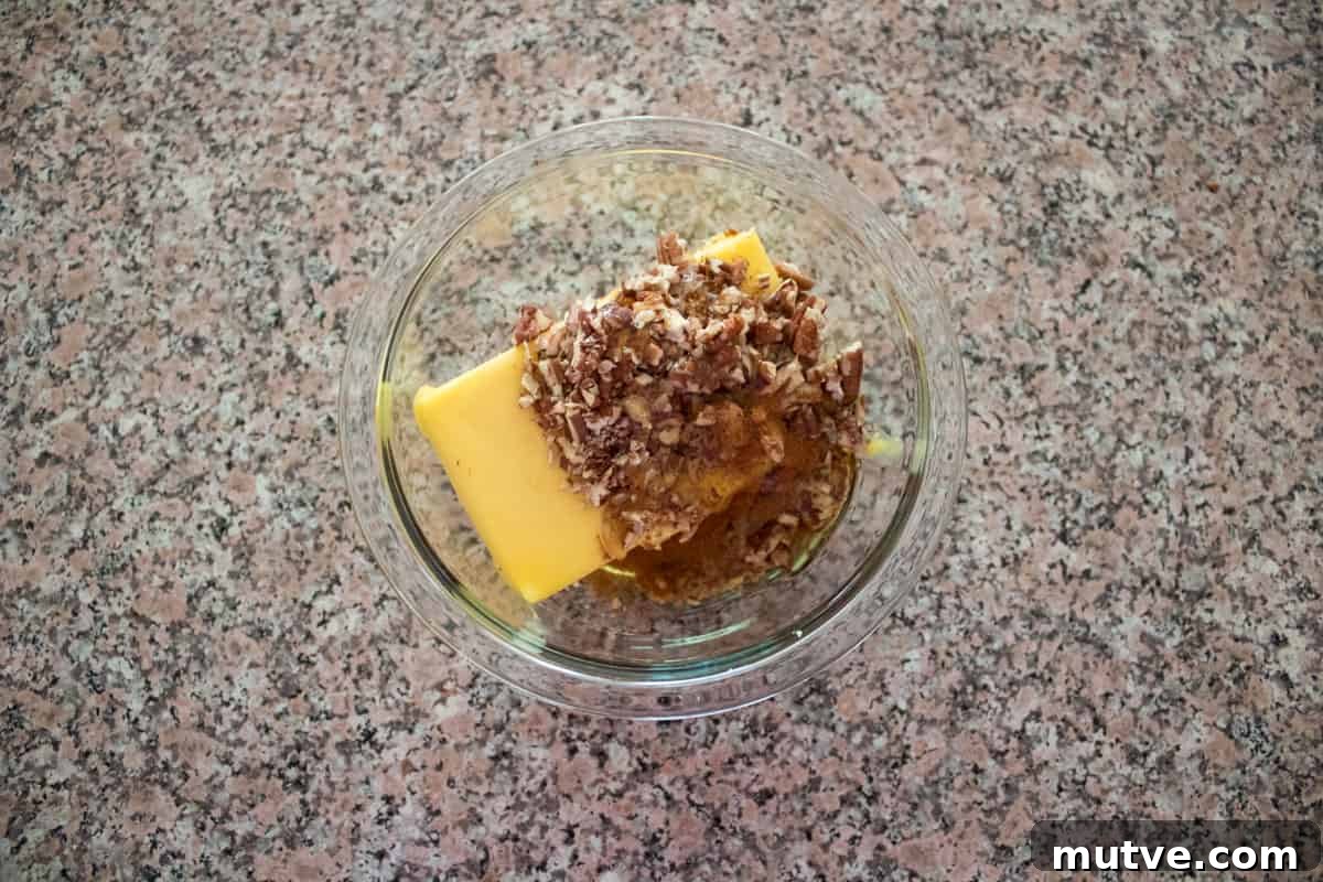 Butter, honey, pecans, and cinnamon in a glass bowl on a kitchen counter.