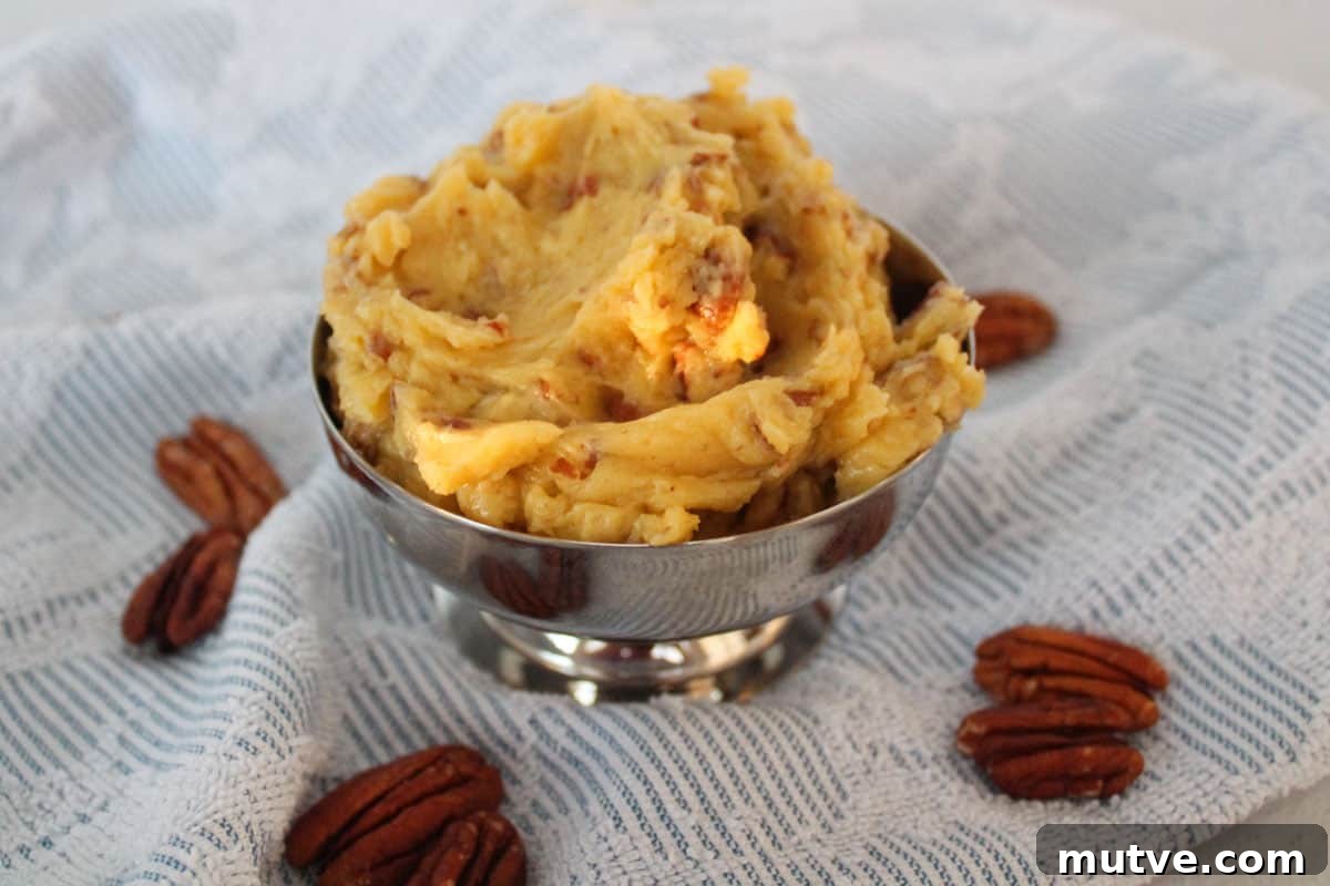 Honey pecan butter in a silver dish sitting on a blue and white towel with pecan halves around it.
