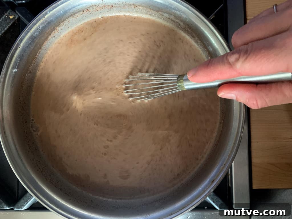 How to Make Mexican Mocha with Authentic Mexican Chocolate 7 A saucepan with a chocolate mixture in it being stirred with a whisk.