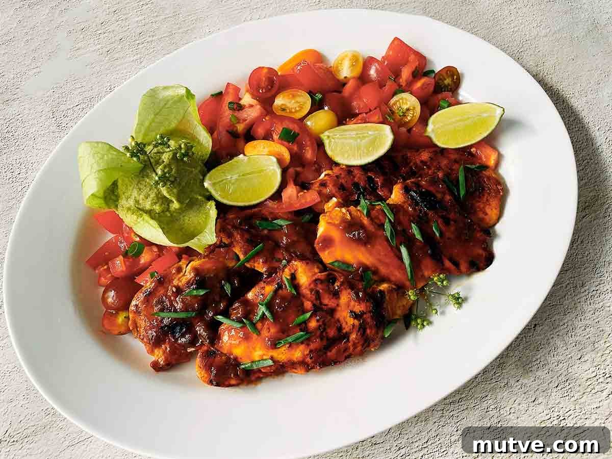 A white platter filled with marinated chicken breasts, tomato salad, and lime wedges.
