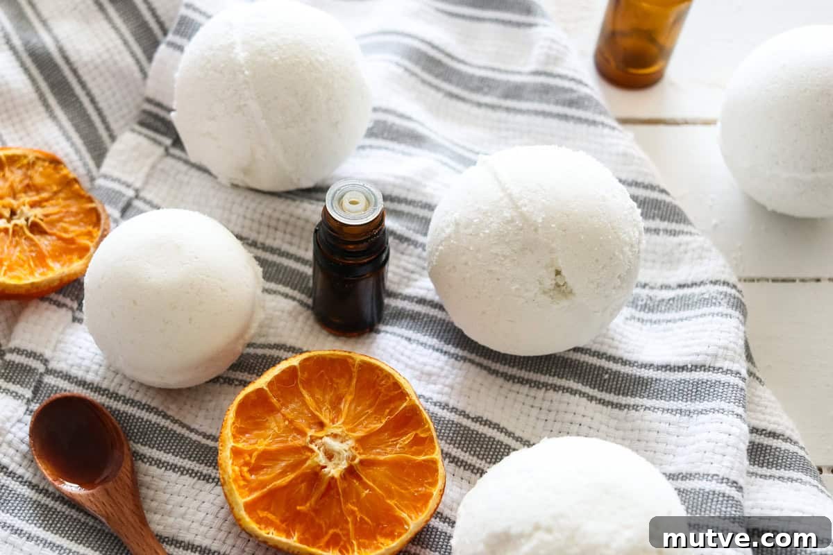 Several homemade bath bombs on a grey and white striped tea towel with dried oranges, essential oil bottles around it.