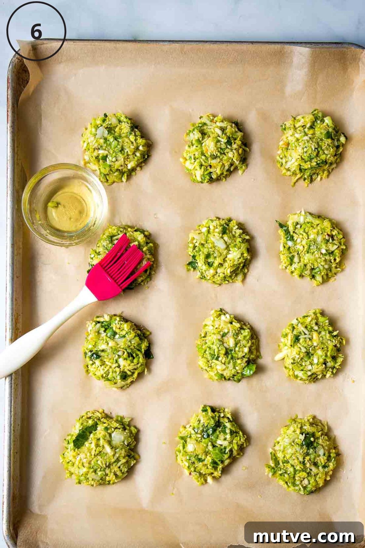 Crispy Oven Baked Brussels Sprouts Latkes 4 Oil being brushed onto Brussels sprouts latkes on a baking sheet lined with parchment.
