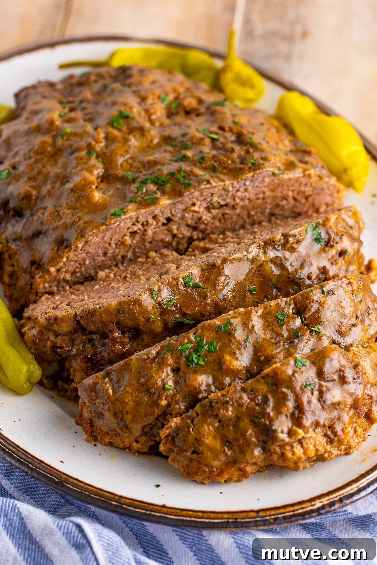 Slow Cooker Mississippi Meatloaf Recipe 2 Mississippi crockpot meatloaf sliced on a platter topped with gravy and a pepperoncini pepper.