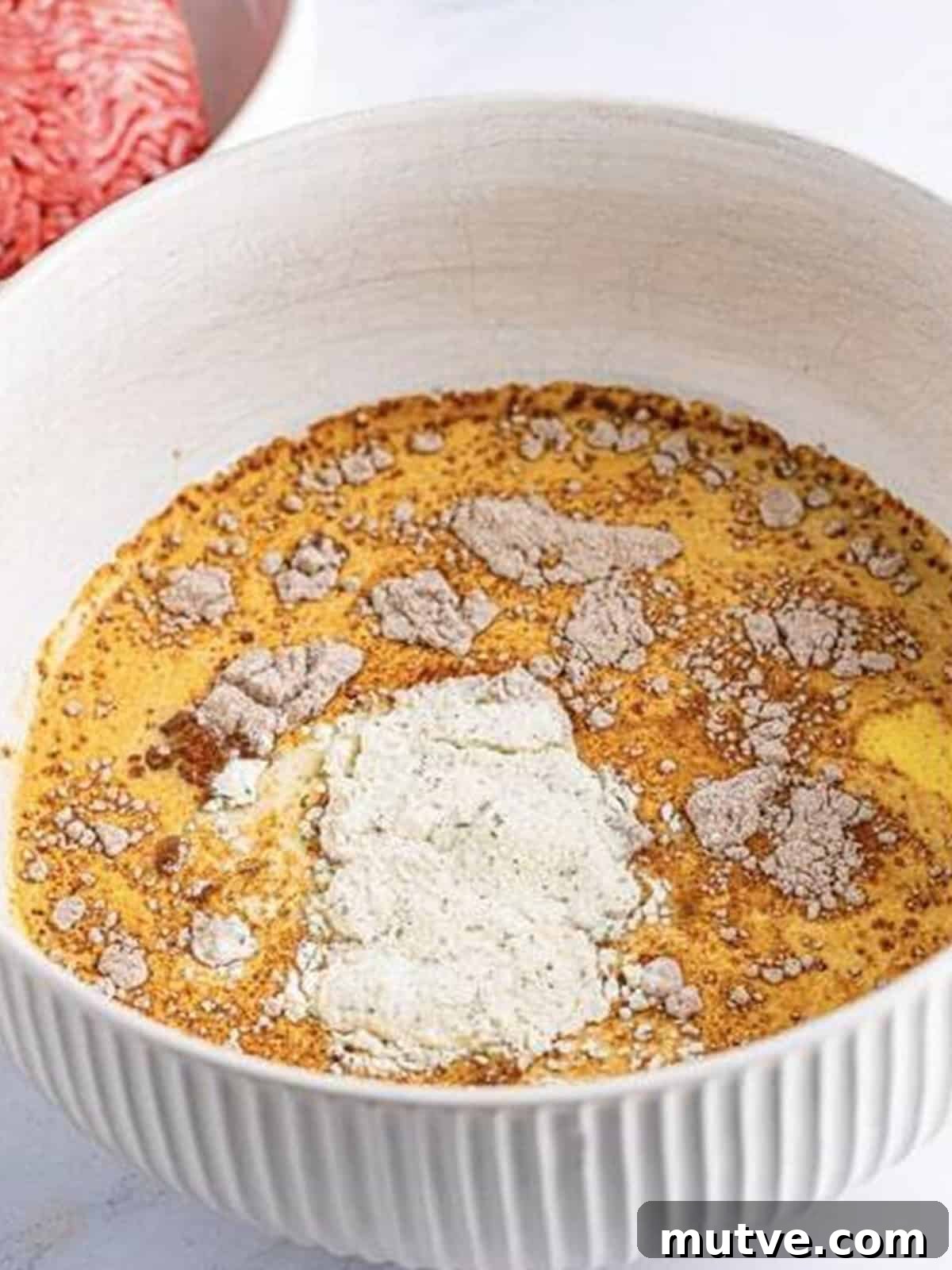 Slow Cooker Mississippi Meatloaf Recipe 4 Milk, eggs, sugar, au jus mix, and ranch seasoning added to a large white bowl for crockpot meatloaf.