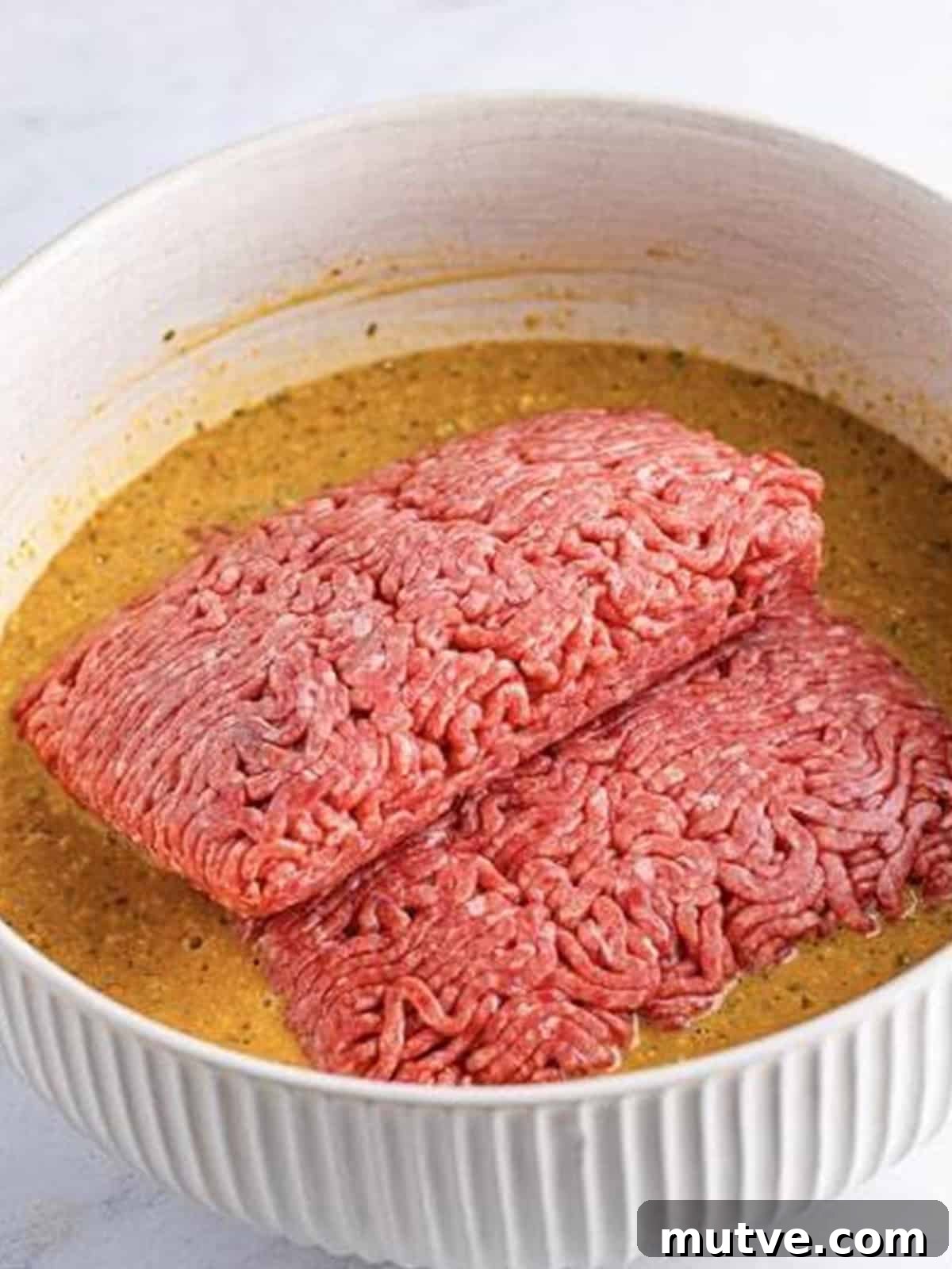 Slow Cooker Mississippi Meatloaf Recipe 7 Lean ground beef added to the meatloaf base mixture in a white bowl.