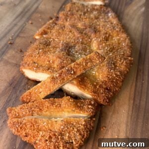 A breaded and fried cutlet, sliced into strips, sits on a wooden surface.