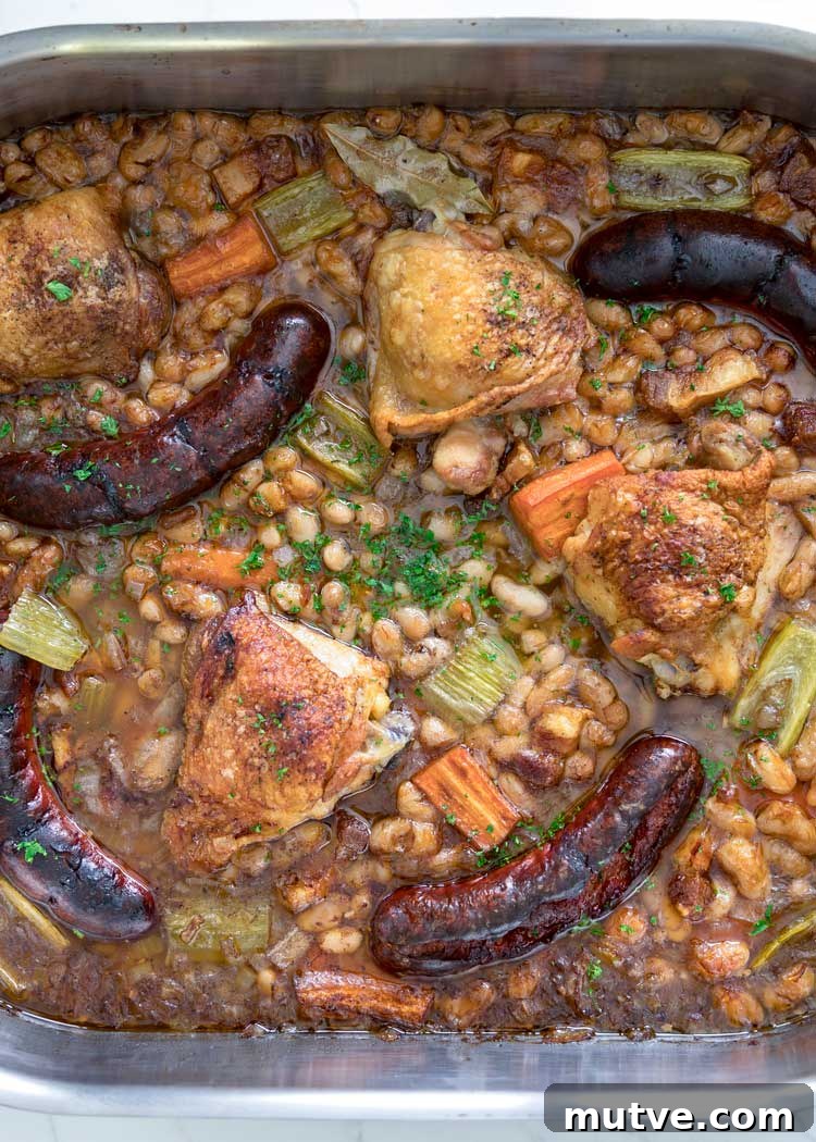 This comforting French Cassoulet recipe has juicy chicken, sausage, bacon and white beans that simmer away in a broth spiked with onion, garlic and herbs. over head shot of roasted sausages, chicken and white beans