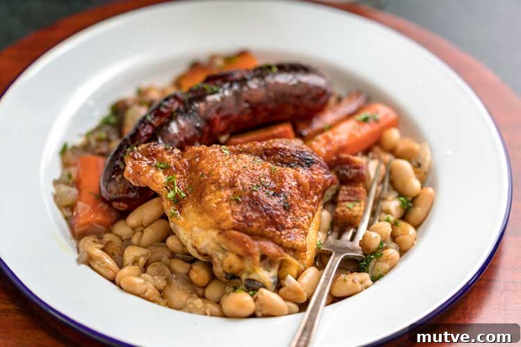 This comforting French Cassoulet recipe has juicy chicken, sausage, bacon and white beans that simmer away in a broth spiked with onion, garlic and herbs. plate of Easy French Cassoulet Recipe