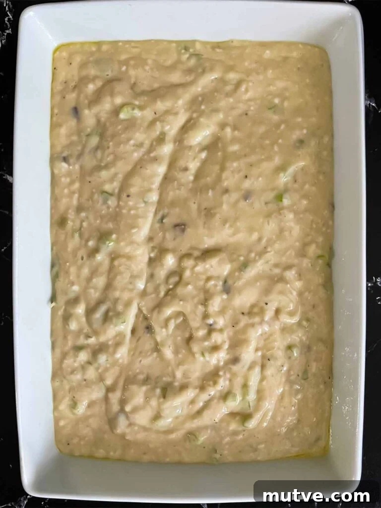 Soup and rice mixture for chicken and rice casserole in a light baking pan on a dark surface.