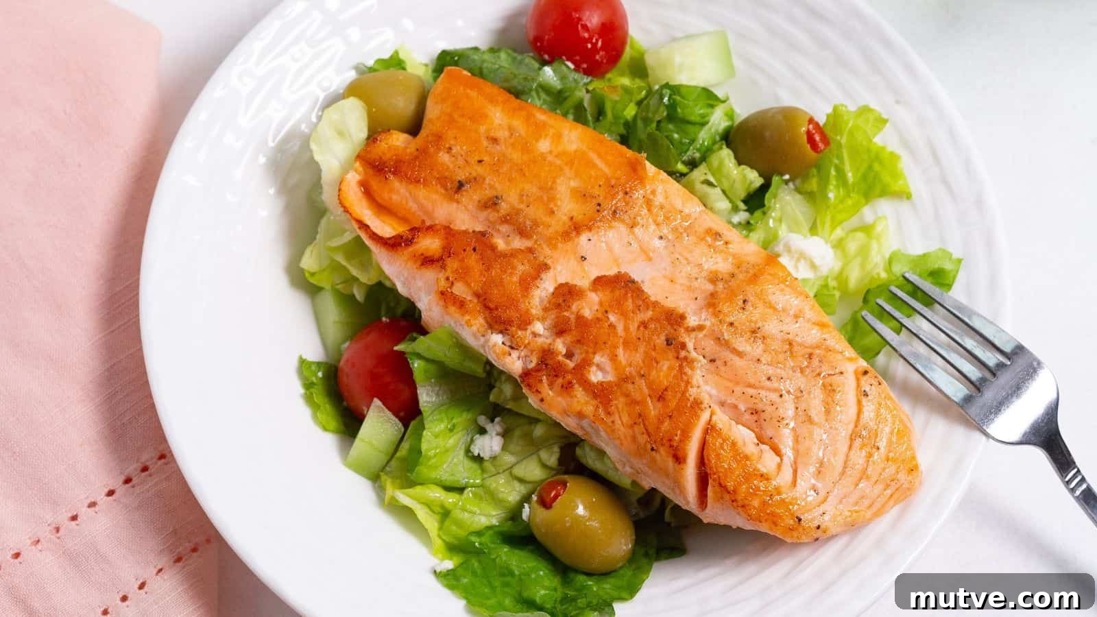 40 End-of-Summer Cookout Recipes to Celebrate Summer's Finale 12 Grilled salmon fillet on top of a fresh green salad with tomatoes and olives, served on a white plate with a fork on the side.