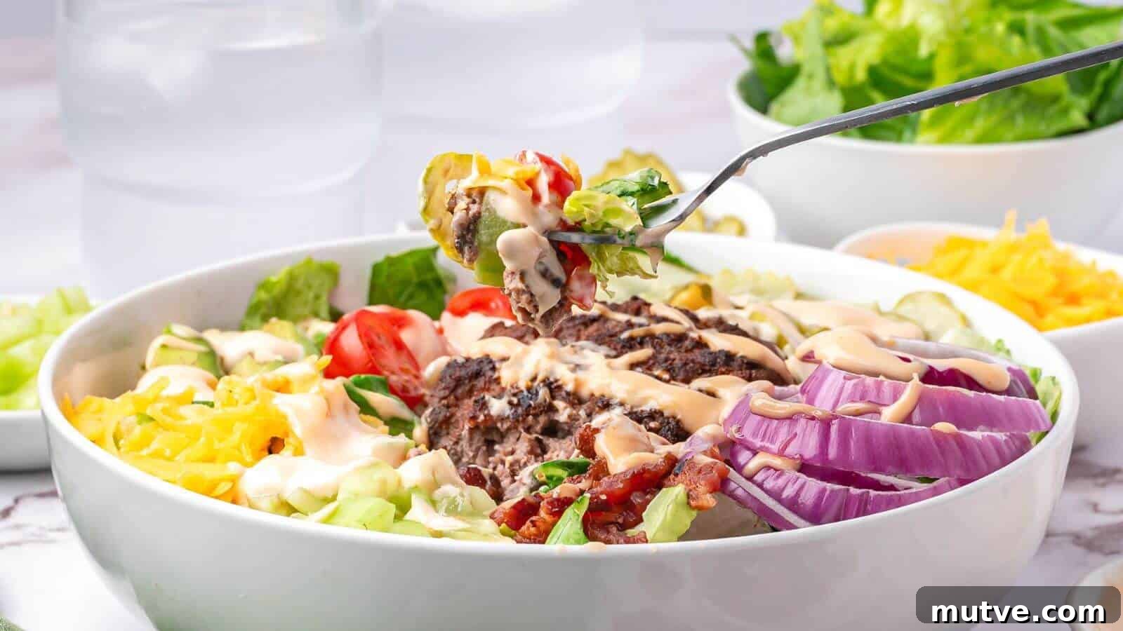 40 End-of-Summer Cookout Recipes to Celebrate Summer's Finale 19 A bowl of salad with hamburger patty, sliced red onion, cherry tomatoes, shredded cheese, pickles, bacon, and dressing; a fork holds a bite above the bowl.