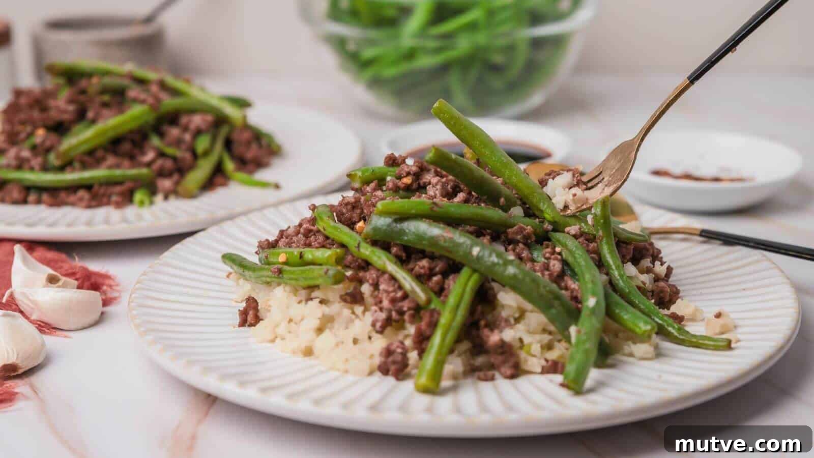 40 End-of-Summer Cookout Recipes to Celebrate Summer's Finale 21 Plate with ground beef, green beans, and cauliflower rice. Fork on the plate, garlic cloves nearby, and a bowl of green beans in the background.