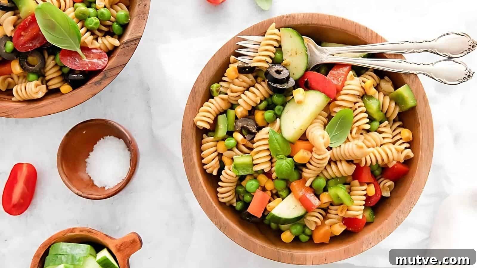 40 End-of-Summer Cookout Recipes to Celebrate Summer's Finale 28 A wooden bowl of pasta salad with rotini, black olives, corn, peas, cucumber, bell peppers, and tomato, garnished with basil. Forks rest on the bowl's rim.