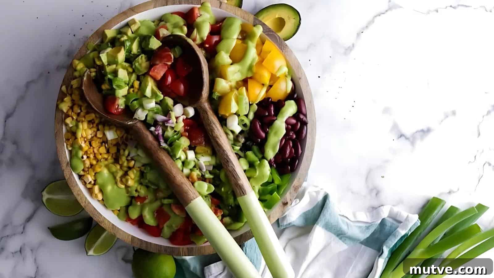 40 End-of-Summer Cookout Recipes to Celebrate Summer's Finale 29 A bowl of chopped vegetables, including tomatoes, corn, avocado, beans, onions, and peppers, topped with green dressing, with two wooden spoons on top.