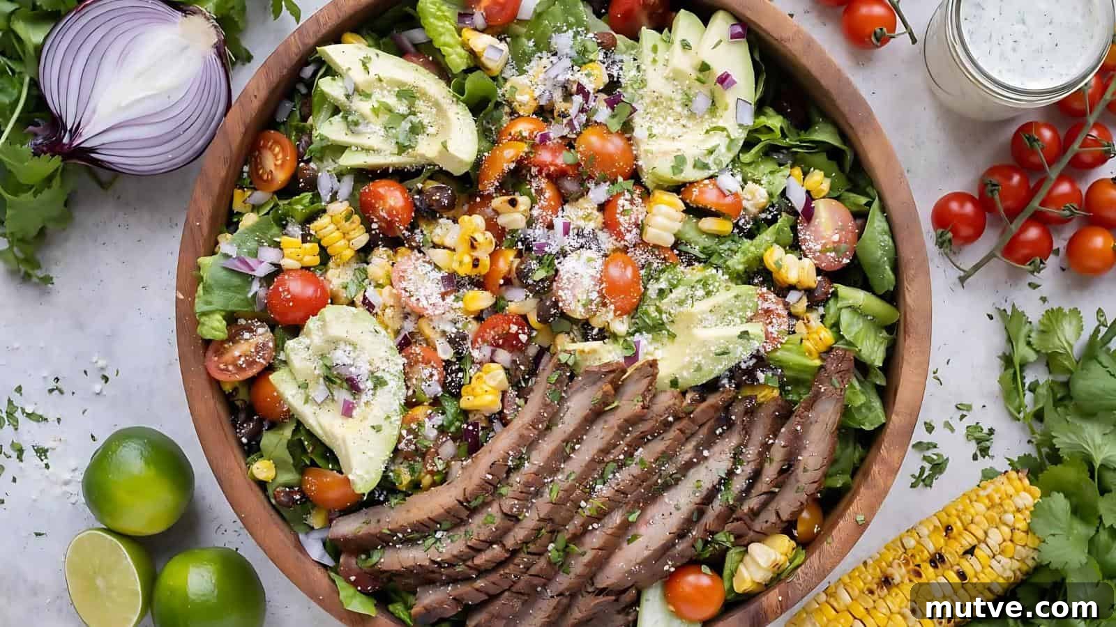40 End-of-Summer Cookout Recipes to Celebrate Summer's Finale 30 A bowl of salad with sliced steak, avocado, cherry tomatoes, corn, red onion, lettuce, and cheese, garnished with herbs. Fresh limes, tomatoes, and corn surround the bowl.