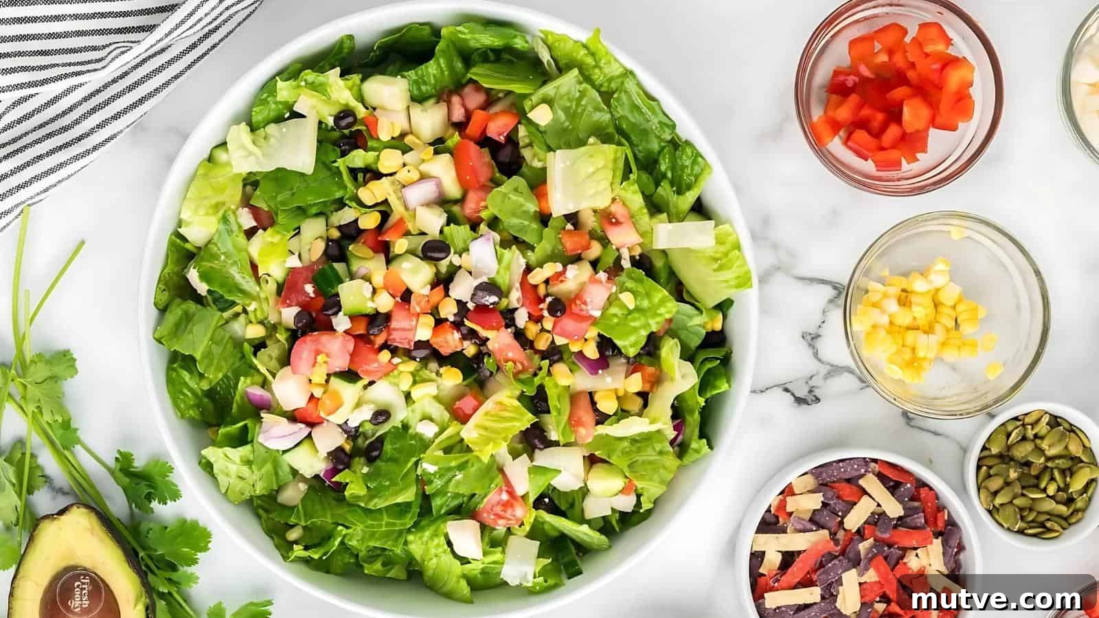 40 End-of-Summer Cookout Recipes to Celebrate Summer's Finale 31 A bowl of chopped salad with lettuce, black beans, corn, tomatoes, onions, and cheese, surrounded by small bowls of ingredients on a white countertop.