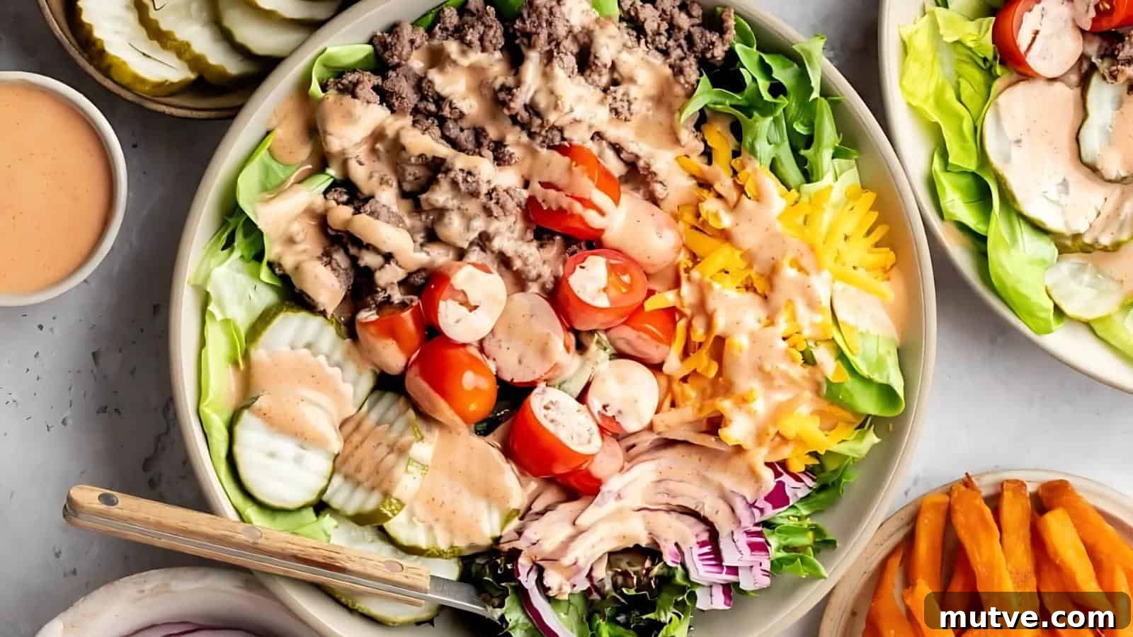 40 End-of-Summer Cookout Recipes to Celebrate Summer's Finale 34 A bowl of salad with ground beef, sliced cherry tomatoes, shredded cheese, pickles, red onions, lettuce, and dressing, served with a fork.
